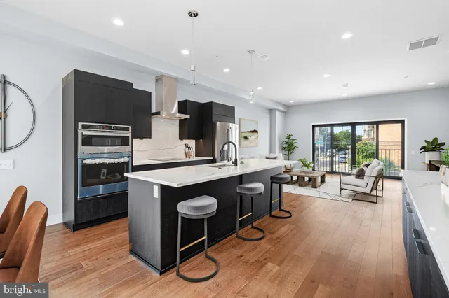 a kitchen with stainless steel appliances granite countertop a stove top oven a sink dishwasher a dining table and chairs with wooden floor