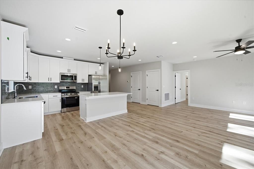 15212 Hawley Road Weeki Wachee, FL 34614 - Photo 11 of 25 a large kitchen with kitchen island a stove a sink dishwasher a refrigerator and white cabinets with wooden floor