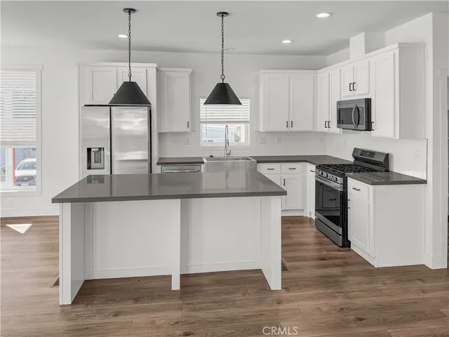 a kitchen with stainless steel appliances granite countertop a sink a stove a refrigerator and white cabinets