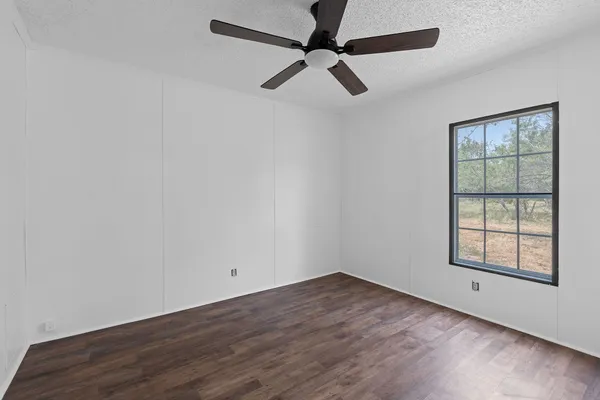 an empty room with wooden floor ceiling fan and windows