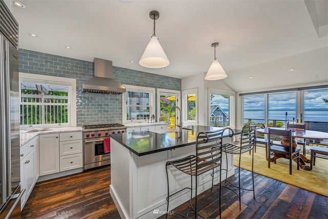 a very nice looking kitchen with granite countertop a stove a sink a dining table and chairs with wooden floor