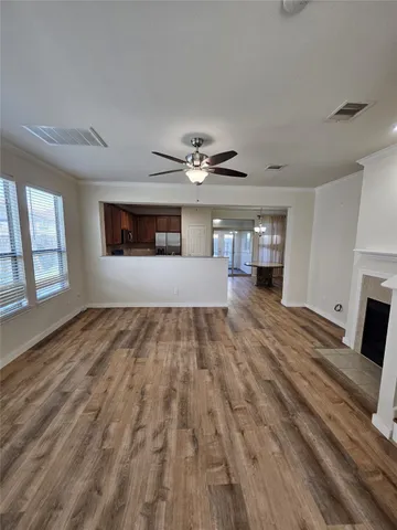 a view of an empty room and a kitchen with wooden floor and a ceiling fan