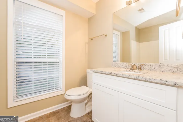 a bathroom with a granite countertop toilet a sink and a mirror