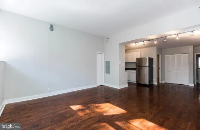 a view of an empty room with wooden floor and a kitchen