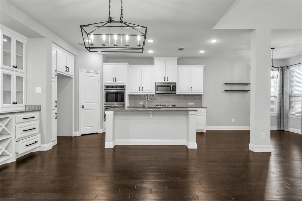 15713 Canyon Ridge Prosper, TX 75078 - Photo 12 of 38 Spacious kitchen featuring an island with counter seating, a built-in oven and microwave, dark wood-finish flooring, white cabinetry with black hardware, and an overhead geometric chandelier