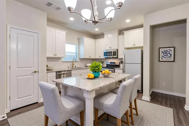 a kitchen with stainless steel appliances kitchen island granite countertop a dining table chairs refrigerator and cabinets