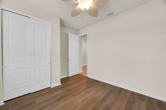 a view of an empty room with wooden floor and a ceiling fan