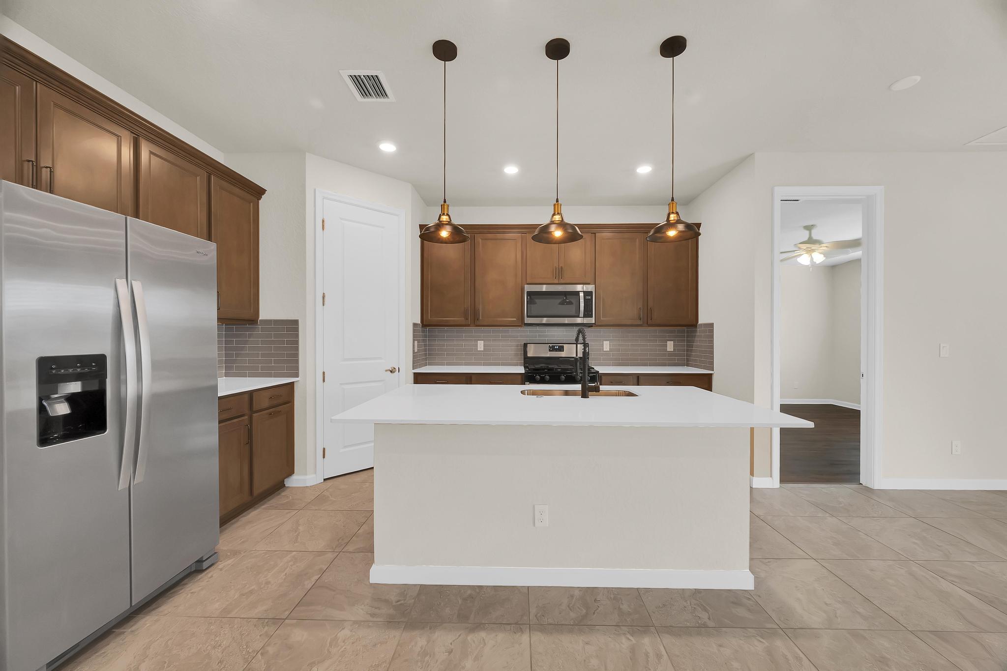 680 Southeast Villandry Way Port St. Lucie, FL 34984 - Photo 4 of 38 a large kitchen with kitchen island a large counter top a sink stainless steel appliances and cabinets