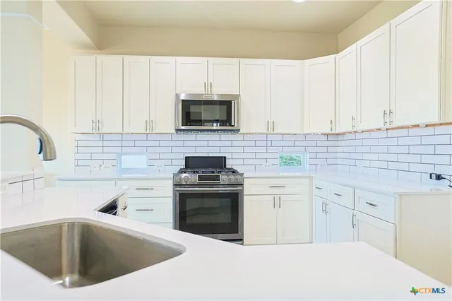 a kitchen with white cabinets a sink and stainless steel appliances