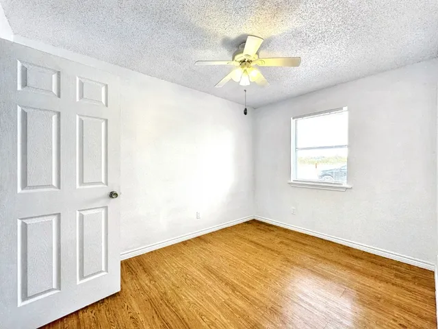 a view of an empty room with wooden floor and a chandelier fan