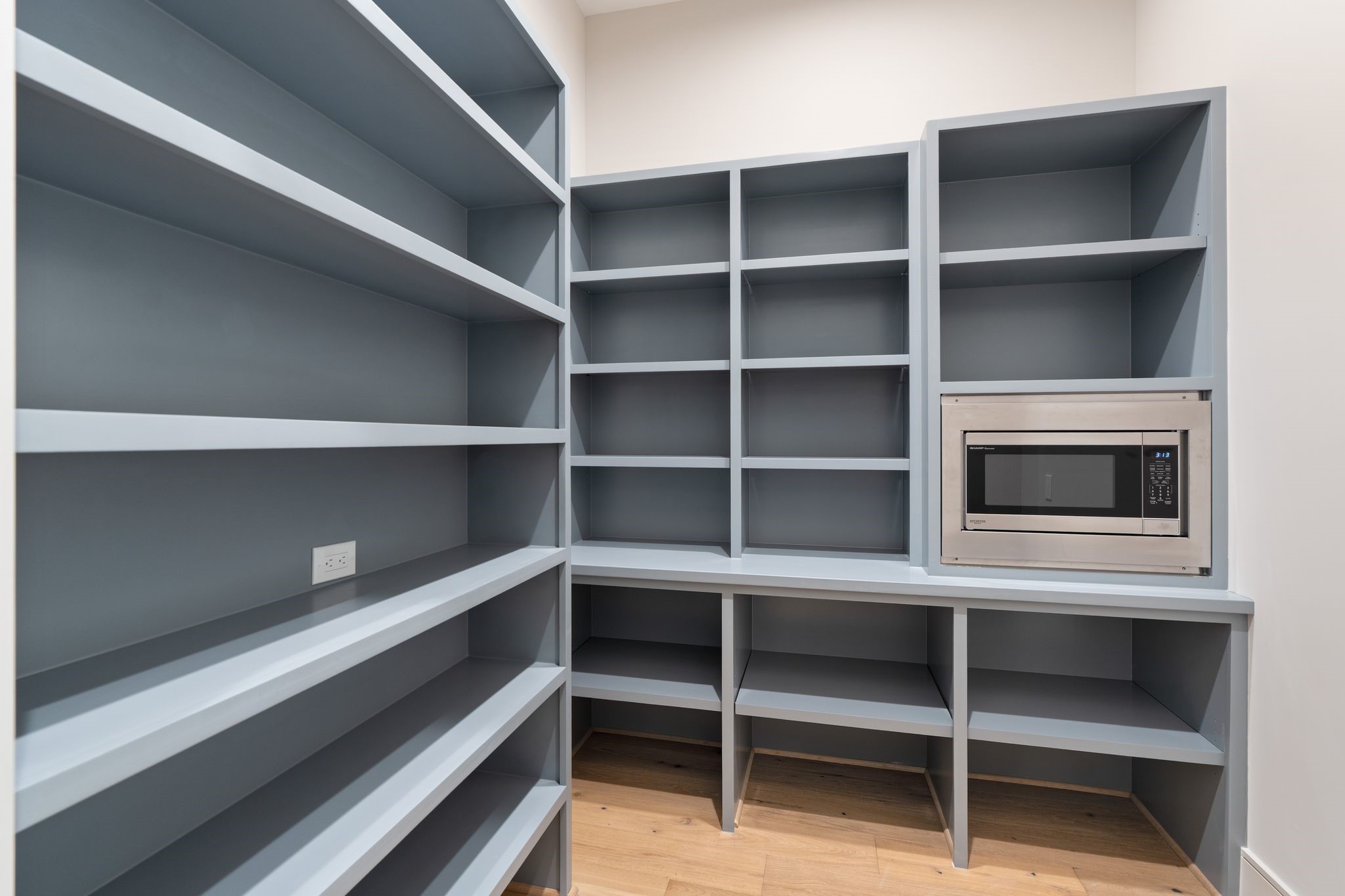 711 East 12th Street Houston, TX 77008 - Photo 24 of 47 This spacious walk-in pantry features extensive shelving in Sherwin-Williams Cadet, a built-in microwave, and outlets for countertop appliances keeping kitchen counters clear and everyday essentials within easy reach.