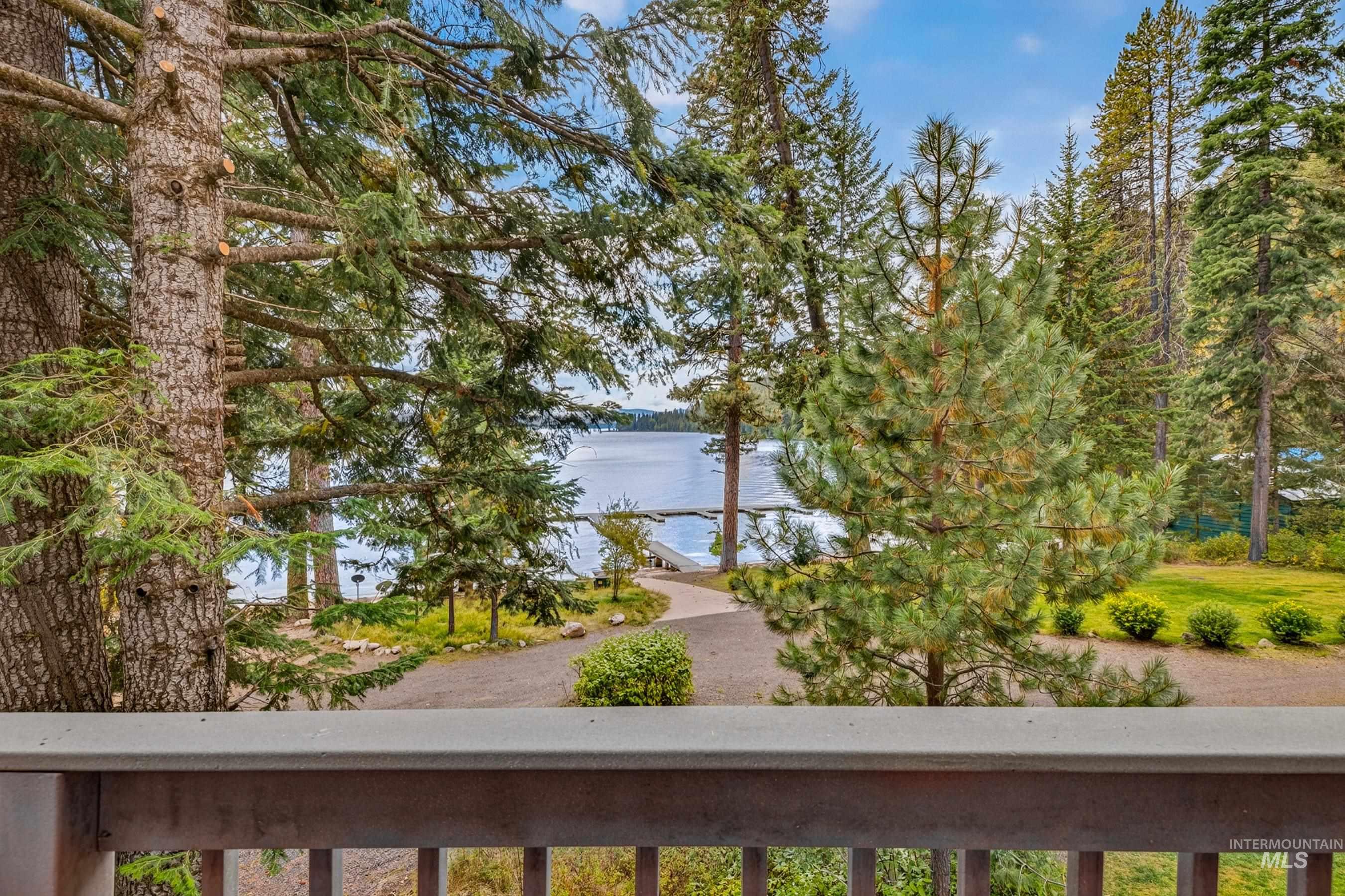 3531 Kp Cove Road McCall, ID 83638 - Photo 6 of 49 Wood-toned railing overlooking a lake with a dock, surrounded by mature evergreen trees and a manicured lawn