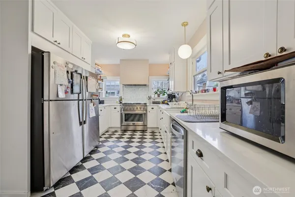a kitchen with stainless steel appliances granite countertop a refrigerator a stove a sink and a oven with white cabinets