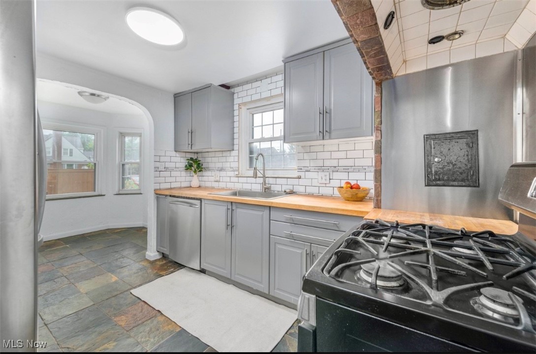 3693 Warren Road Cleveland, OH 44111 - Photo 14 of 37 Kitchen with gray cabinetry, stainless steel appliances, tasteful backsplash, wood counters, and arched walkways