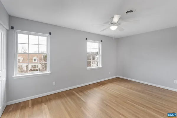 a view of an empty room with wooden floor and a ceiling fan