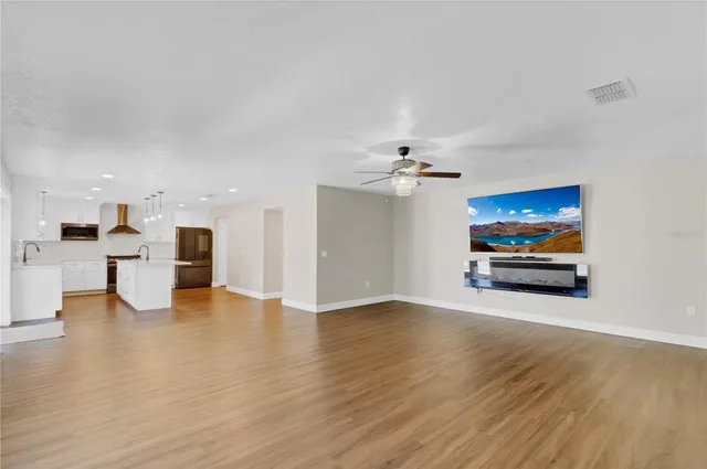 a view of an empty room with wooden floor and a kitchen view