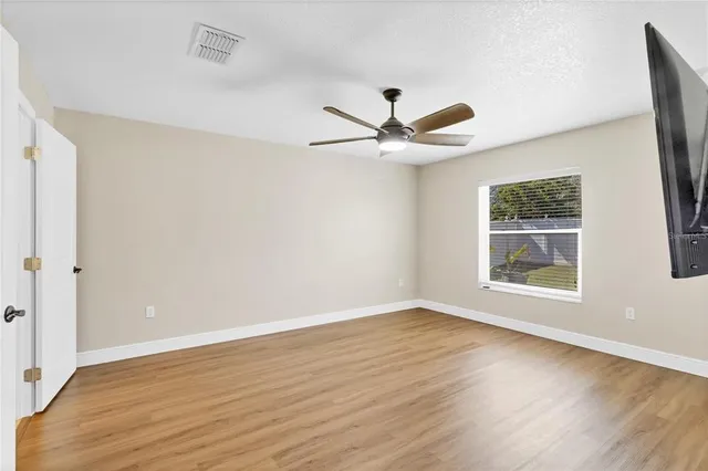 an empty room with wooden floor window and ceiling fan