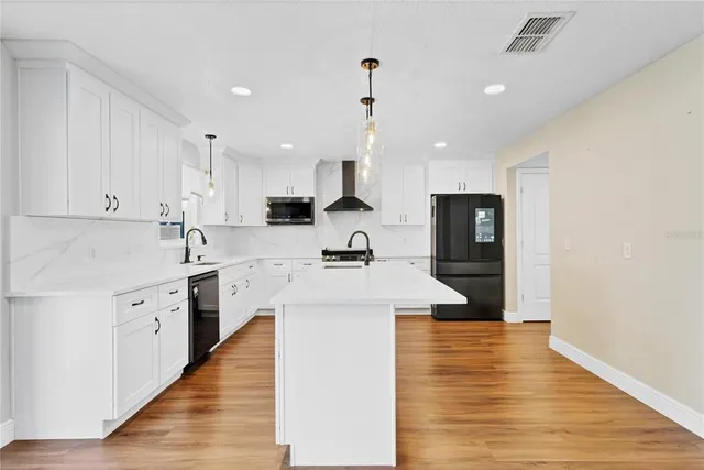 a kitchen with stainless steel appliances kitchen island a sink dishwasher a stove and white cabinets with wooden floor