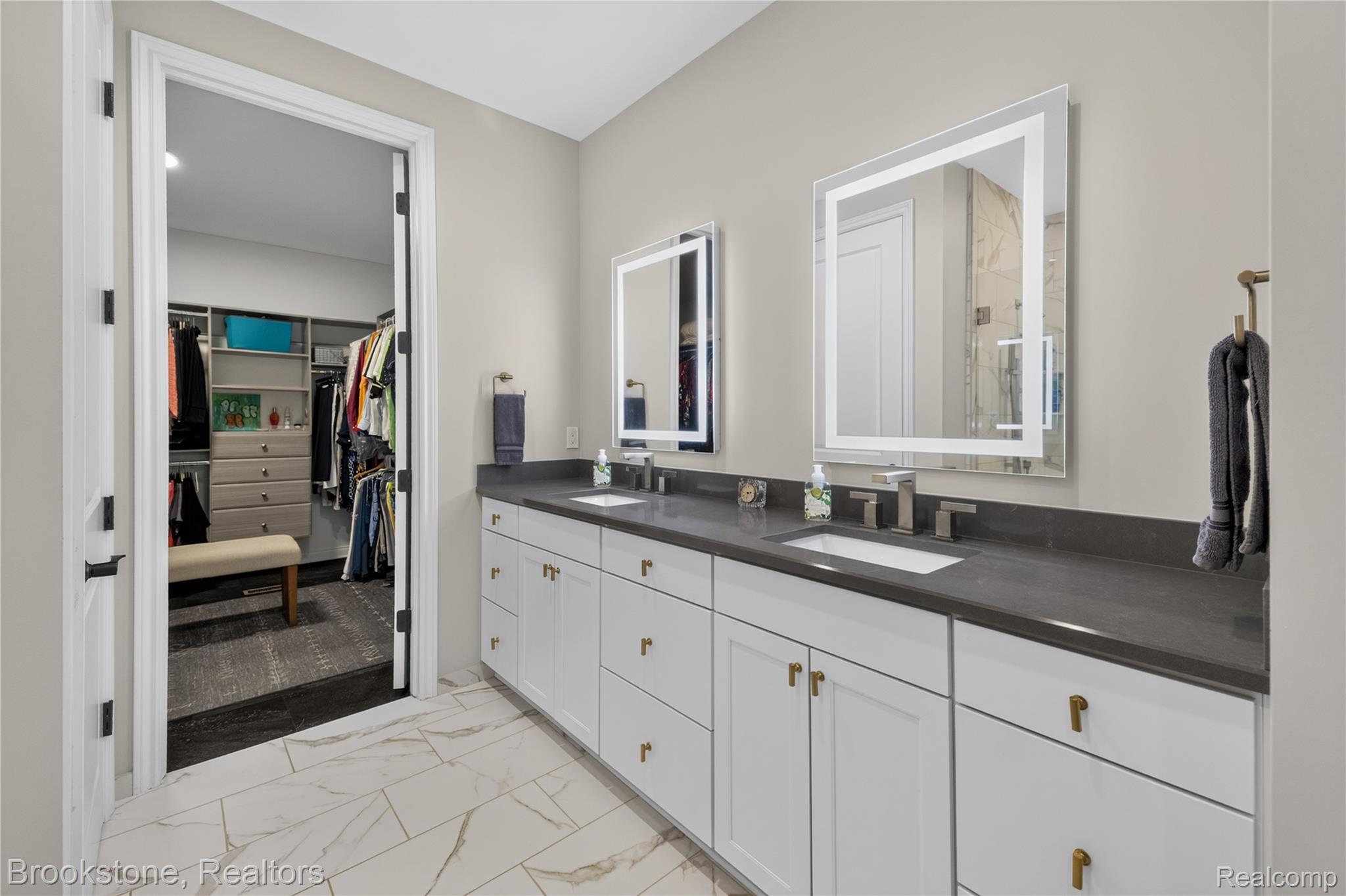 2167 Sanctuary Court Rochester, MI 48309 - Photo 50 of 68 Dual sink vanity featuring a dark countertop, white cabinetry with brass hardware, and two illuminated mirrors