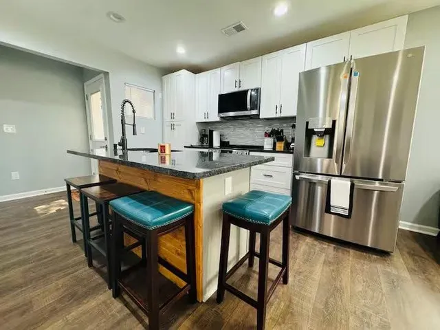 a kitchen with stainless steel appliances granite countertop a refrigerator a stove a sink dishwasher a dining table and chairs with wooden floor
