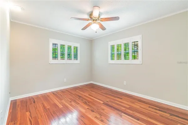 an empty room with wooden floor fan and windows