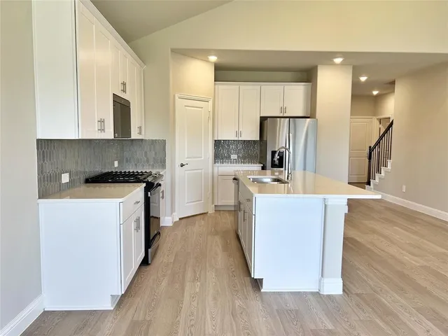 a living room with stainless steel appliances kitchen island granite countertop wooden floors and white cabinets