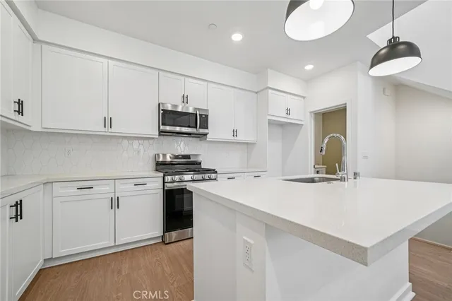 a kitchen with stainless steel appliances granite countertop a sink a stove a refrigerator a white stove with white cabinets and wooden floor