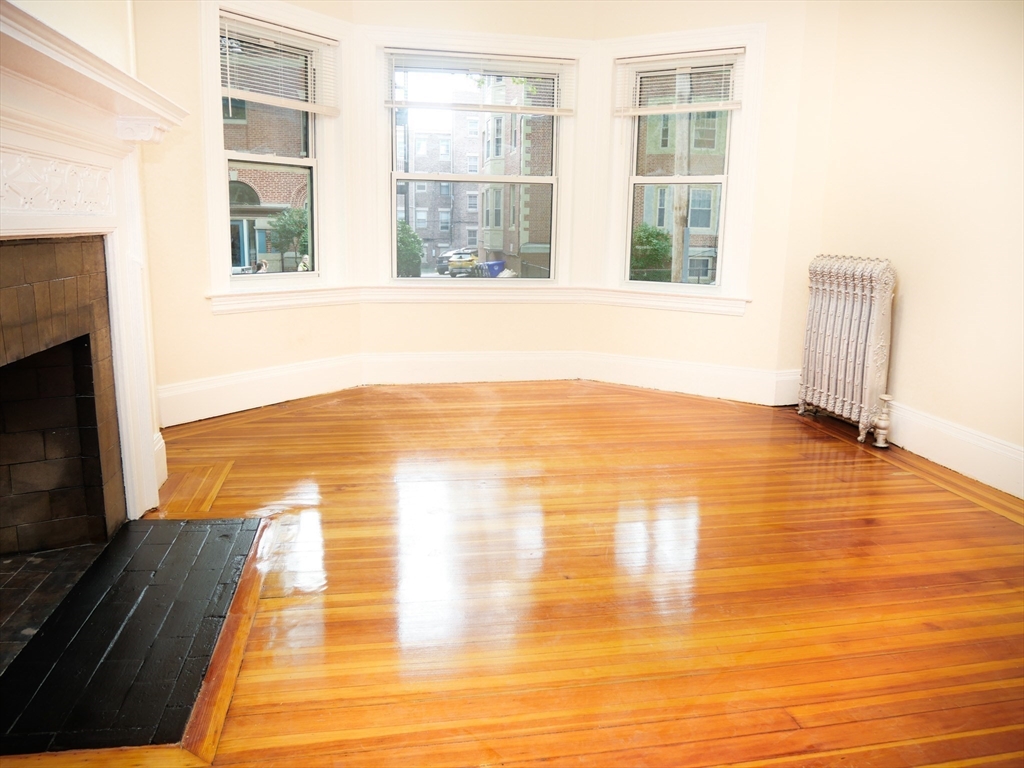 a view of an empty room with wooden floor and a fireplace