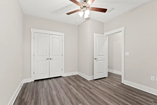 an empty room with wooden floor closet and windows