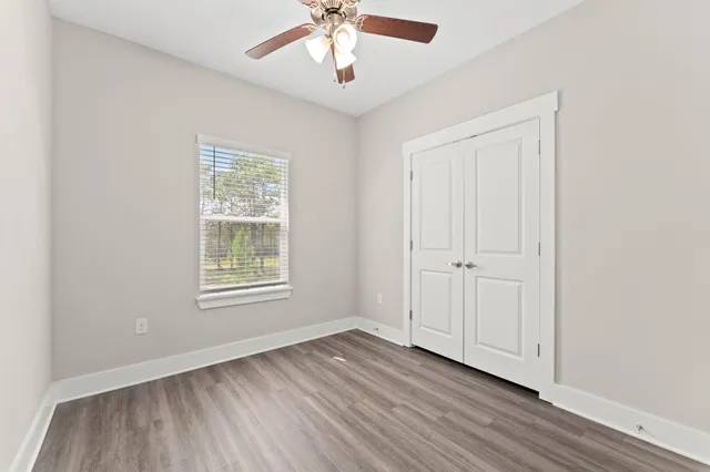 an empty room with wooden floor chandelier fan and windows