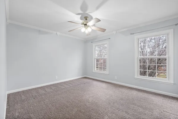 an empty room with chandelier fan and windows