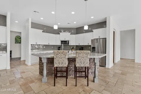 a kitchen with kitchen island granite countertop a dining table chairs refrigerator and cabinets
