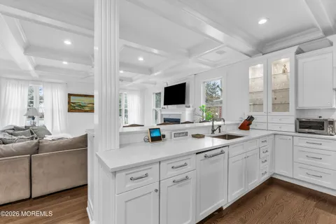 a open white kitchen with stainless steel appliances granite countertop a sink and white cabinets with wooden floor