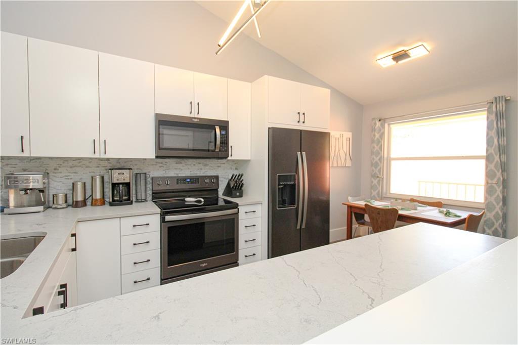 225 Robin Hood Circle, Unit 203 Naples, FL 34104 - Photo 16 of 50 Kitchen featuring light stone counters, stainless steel appliances, tasteful backsplash, white cabinets, and lofted ceiling