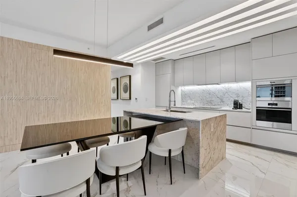 a kitchen with stainless steel appliances kitchen island a table chairs in it and white cabinets
