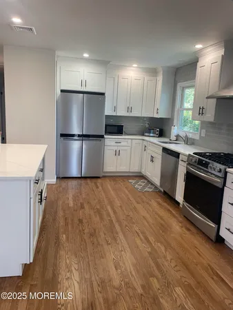 a kitchen with stainless steel appliances granite countertop a refrigerator a stove a sink and white cabinets