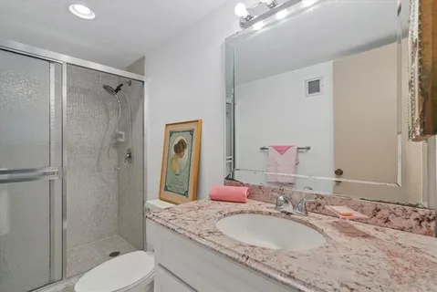 a bathroom with a granite countertop shower sink vanity mirror and toilet