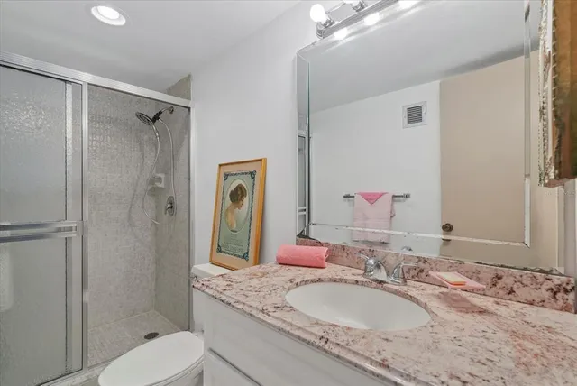 a bathroom with a granite countertop shower sink vanity mirror and toilet