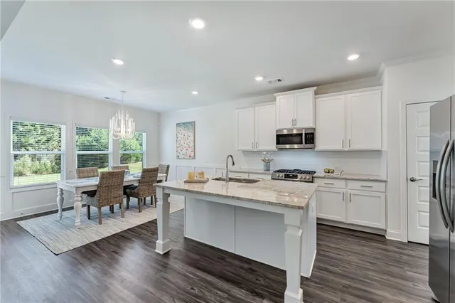 a kitchen with stainless steel appliances granite countertop a stove top oven a sink dishwasher a dining table and chairs with wooden floor