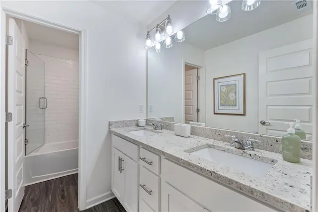 a bathroom with a granite countertop double vanity sink a mirror and shower