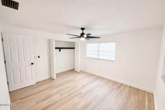 an empty room with wooden floor ceiling fan and windows