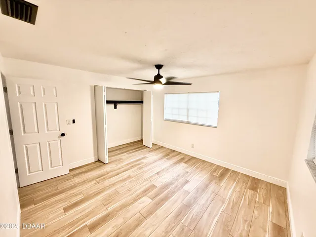 an empty room with wooden floor ceiling fan and windows
