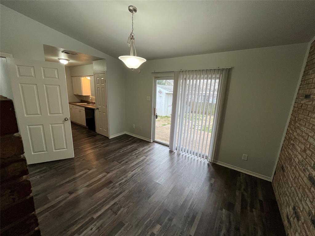 1841 South Perry Road Carrollton, TX 75006 - Photo 6 of 25 Unfurnished dining area with dark wood-style flooring, lofted ceiling, and brick wall
