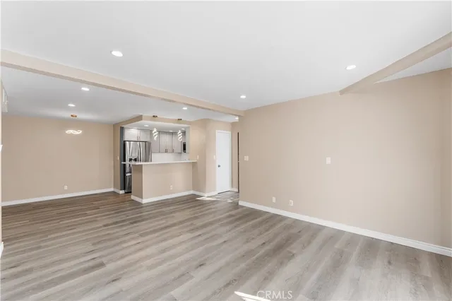 a view of an empty room with wooden floor kitchen view and a window