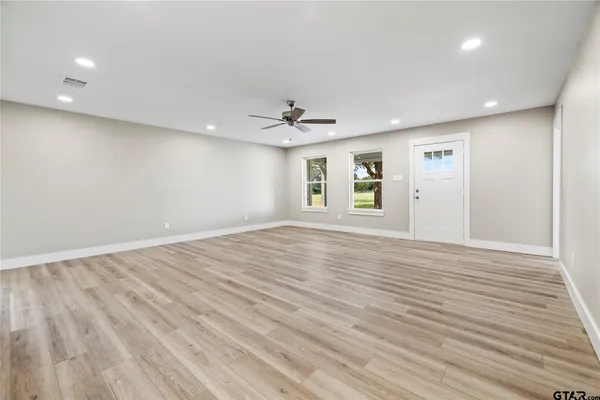 an empty room with wooden floor ceiling fan and windows
