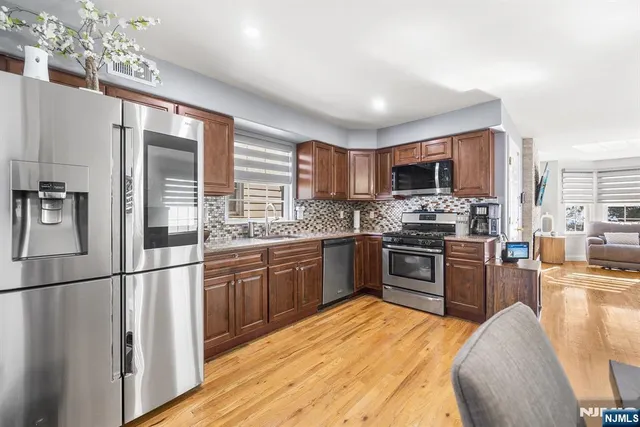 a kitchen with stainless steel appliances granite countertop a refrigerator a stove top oven a sink dishwasher and wooden cabinets with wooden floor