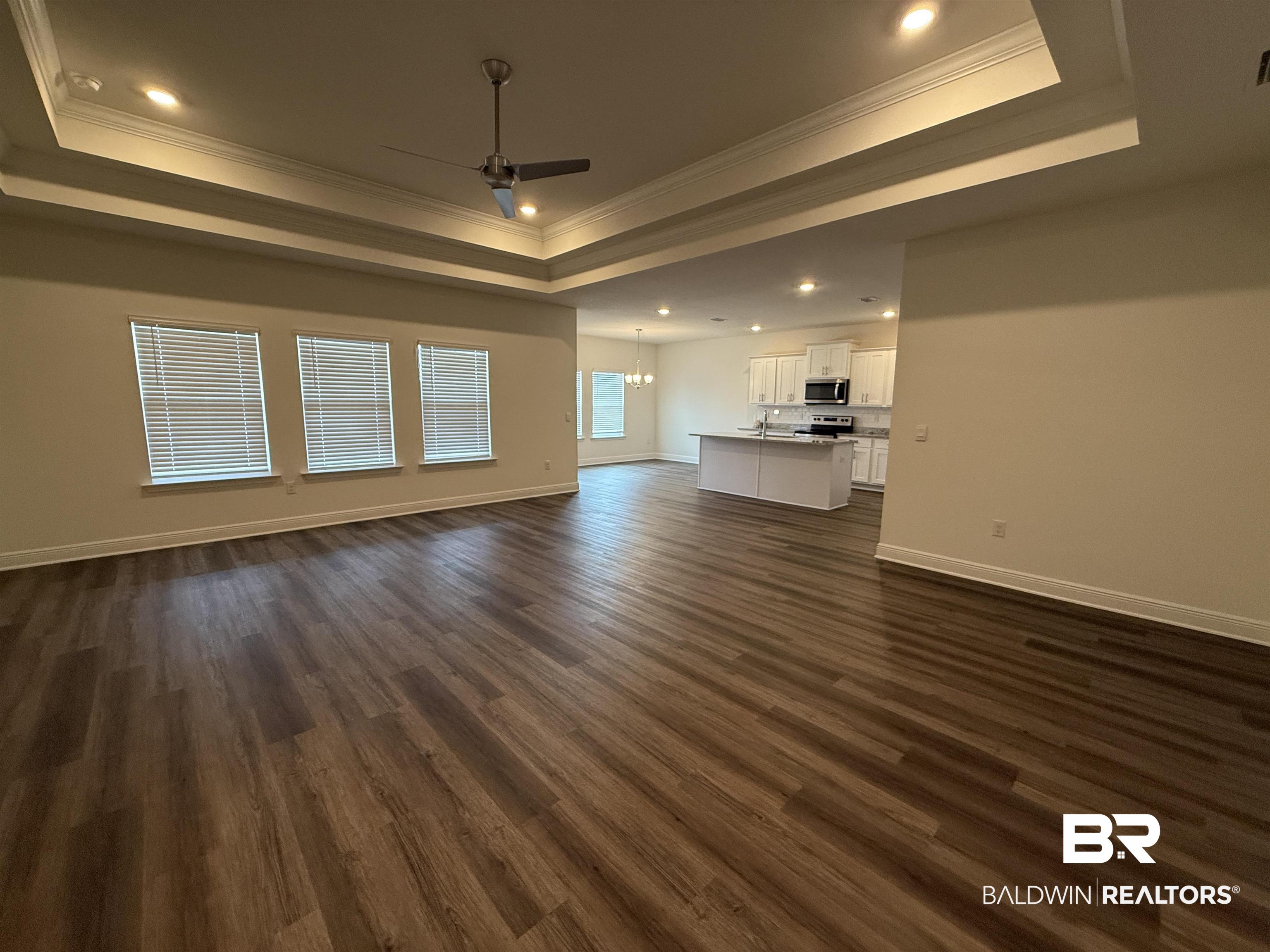 11442 Genuine Risk Circle Daphne, AL 36526 - Photo 2 of 21 Unfurnished living room featuring a ceiling fan, dark wood finished floors, hanging lights, ornamental molding, and a raised ceiling