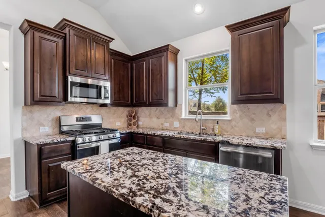 a kitchen with stainless steel appliances granite countertop a stove a sink dishwasher and microwave with wooden cabinets
