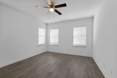 an empty room with wooden floor fan and windows