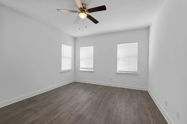 an empty room with wooden floor fan and windows